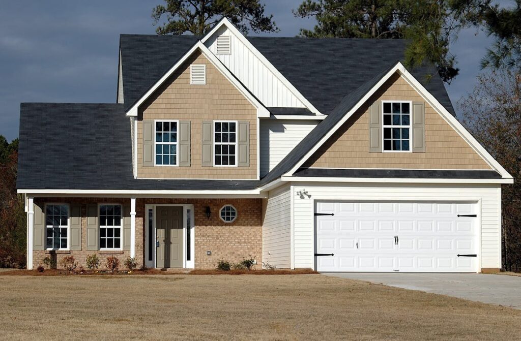 Two-story suburban house with a double garage, beige siding, and a dark shingled roof on a lawn.