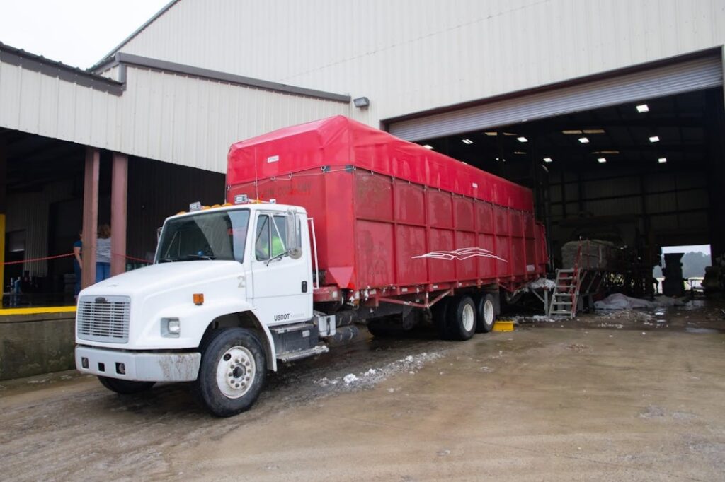 White truck with a large red trailer is parked halfway inside an industrial warehouse with an open garage door.